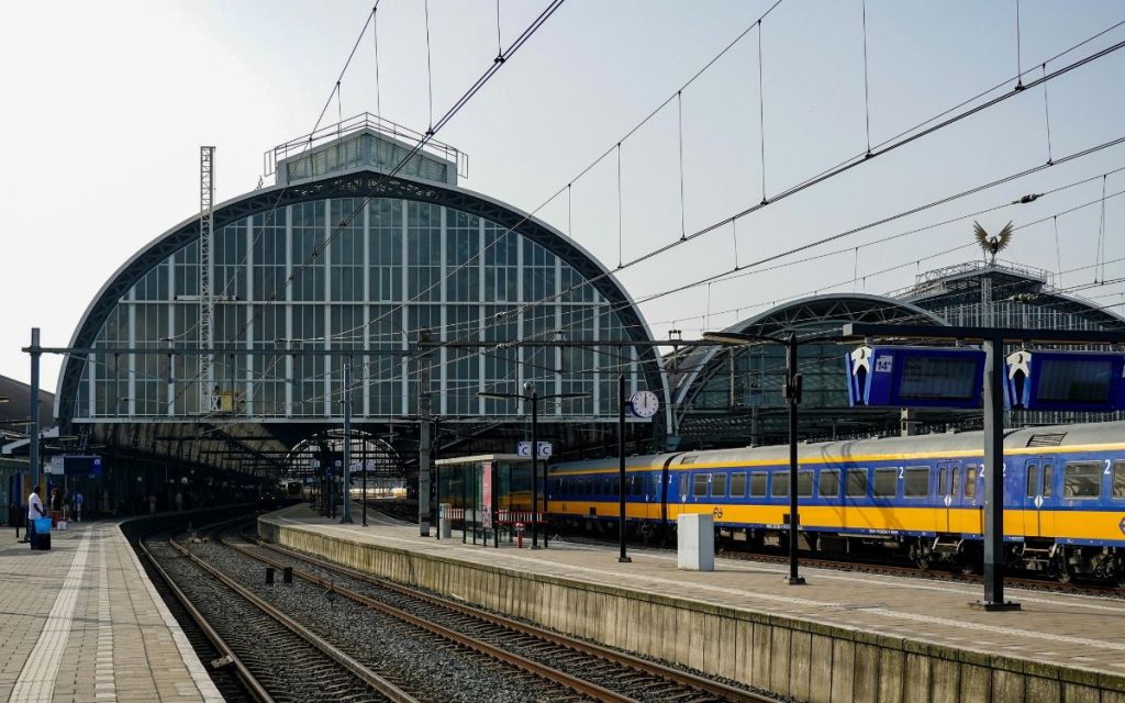Perron van Amsterdam Centraal onder de glazen overkapping, met een NS-trein